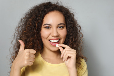 Photo of African-American woman taking vitamin pill on light grey background