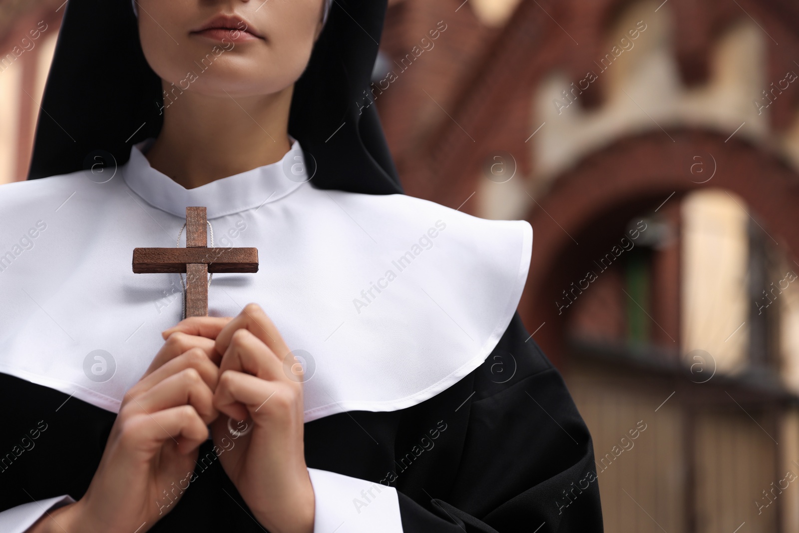 Photo of Young nun holding Christian cross near building outdoors, closeup