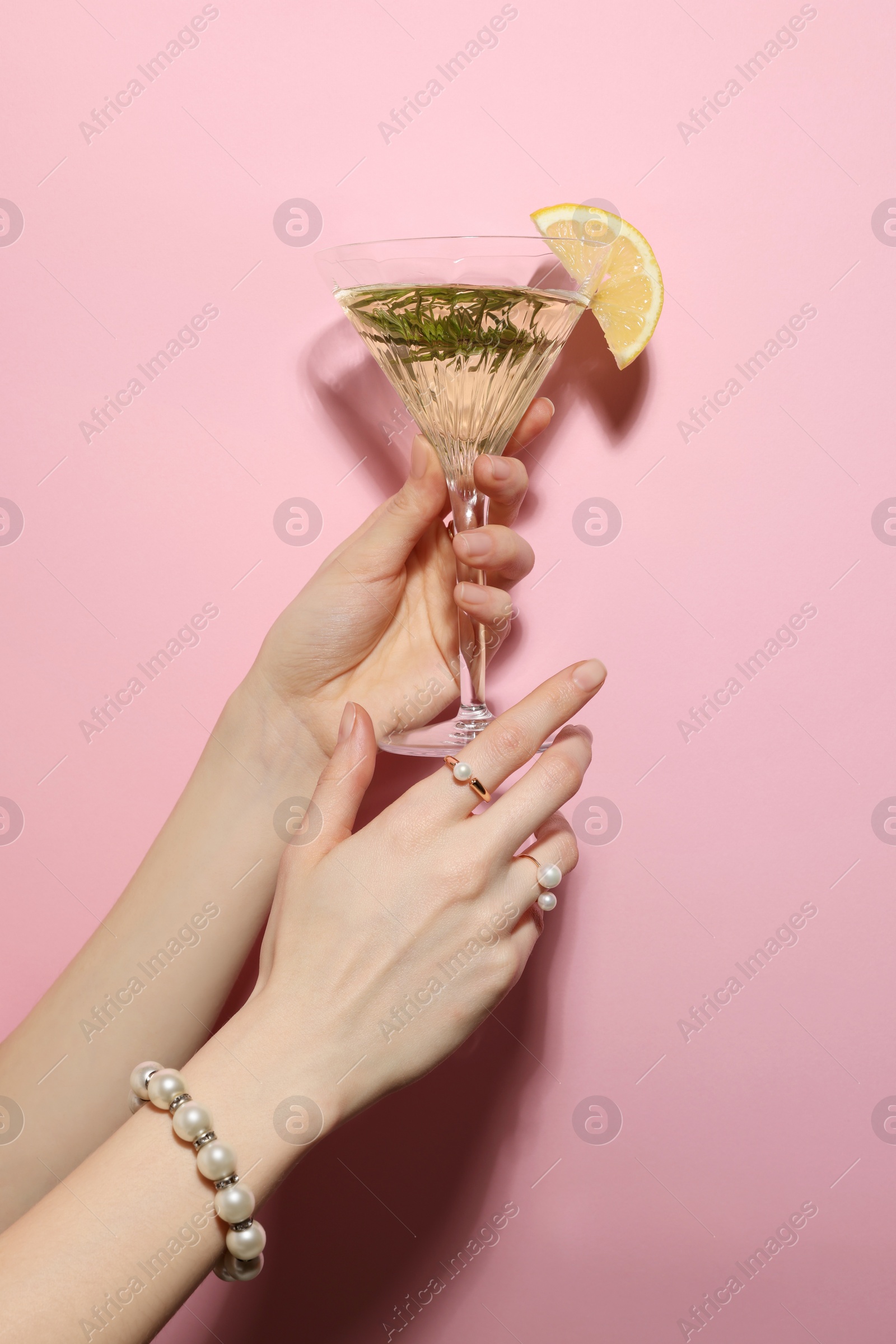 Photo of Woman holding martini glass of refreshing cocktail with lemon slice and rosemary on pink background, closeup