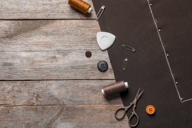 Photo of Set of tailoring accessories and fabric on wooden background, top view