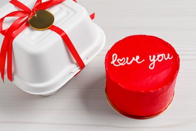 Photo of Bento cake with text Love You and takeaway packaging on white wooden table. St. Valentine's day surprise