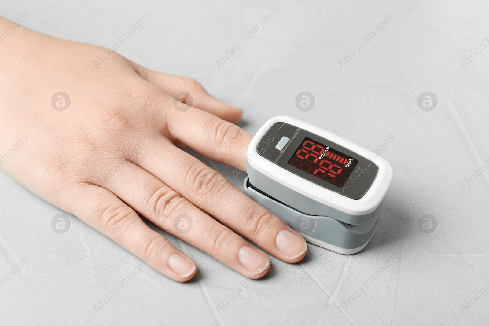Photo of Woman using fingertip pulse oximeter on light grey stone background, closeup