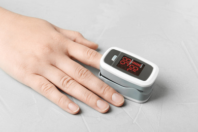 Woman using fingertip pulse oximeter on light grey stone background, closeup