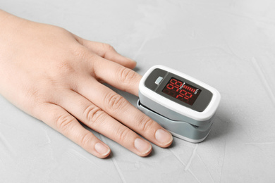 Photo of Woman using fingertip pulse oximeter on light grey stone background, closeup