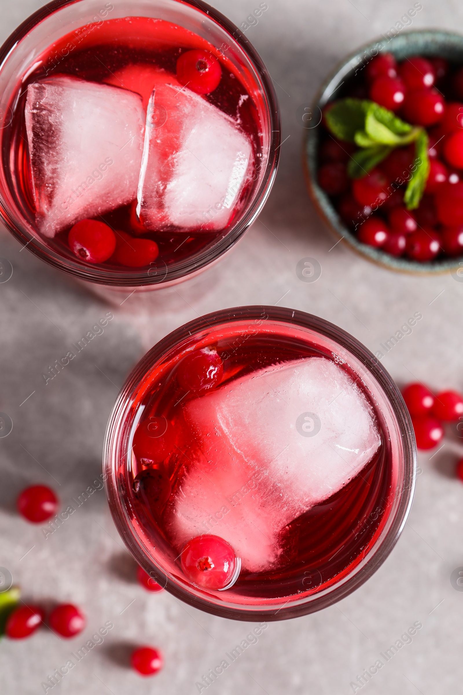 Photo of Tasty cranberry juice with ice cubes in glasses and fresh berries on light grey table, flat lay
