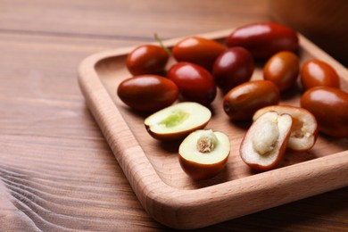 Photo of Wooden plate with fresh Ziziphus jujuba fruits on table, closeup