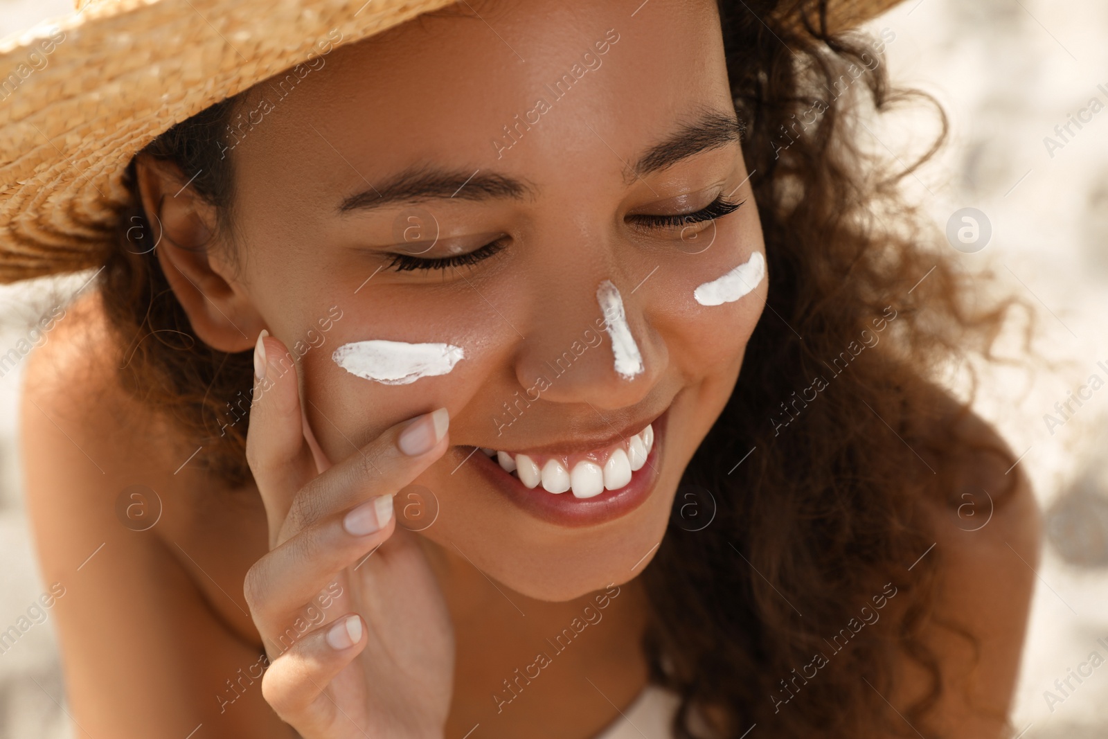 Photo of Beautiful African American woman with sun protection cream on face at sandy beach, closeup