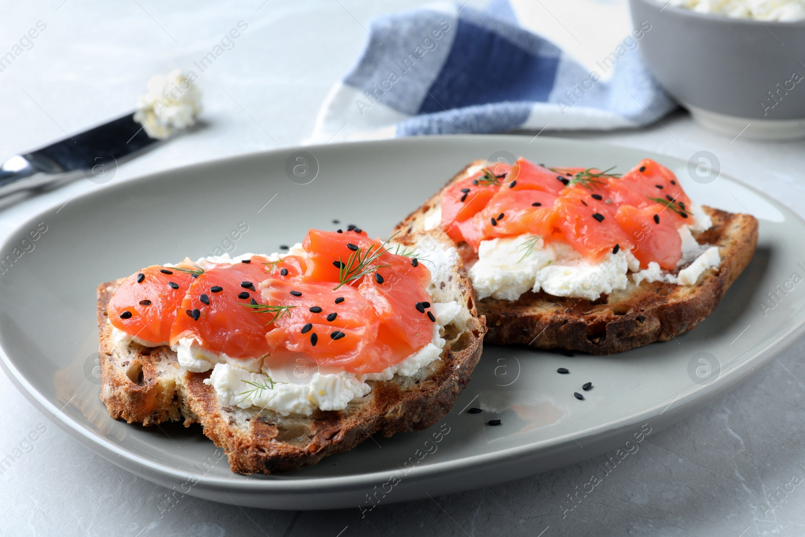 Photo of Delicious sandwiches with cream cheese, salmon and black sesame seeds on light grey table, closeup