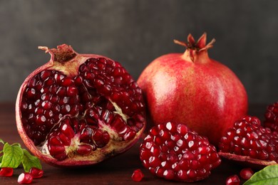 Fresh pomegranates and green leaves on wooden table, closeup
