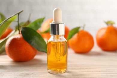 Photo of Bottle of tangerine essential oil and fresh fruits on white wooden table, closeup
