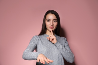 Woman showing HUSH gesture in sign language on color background