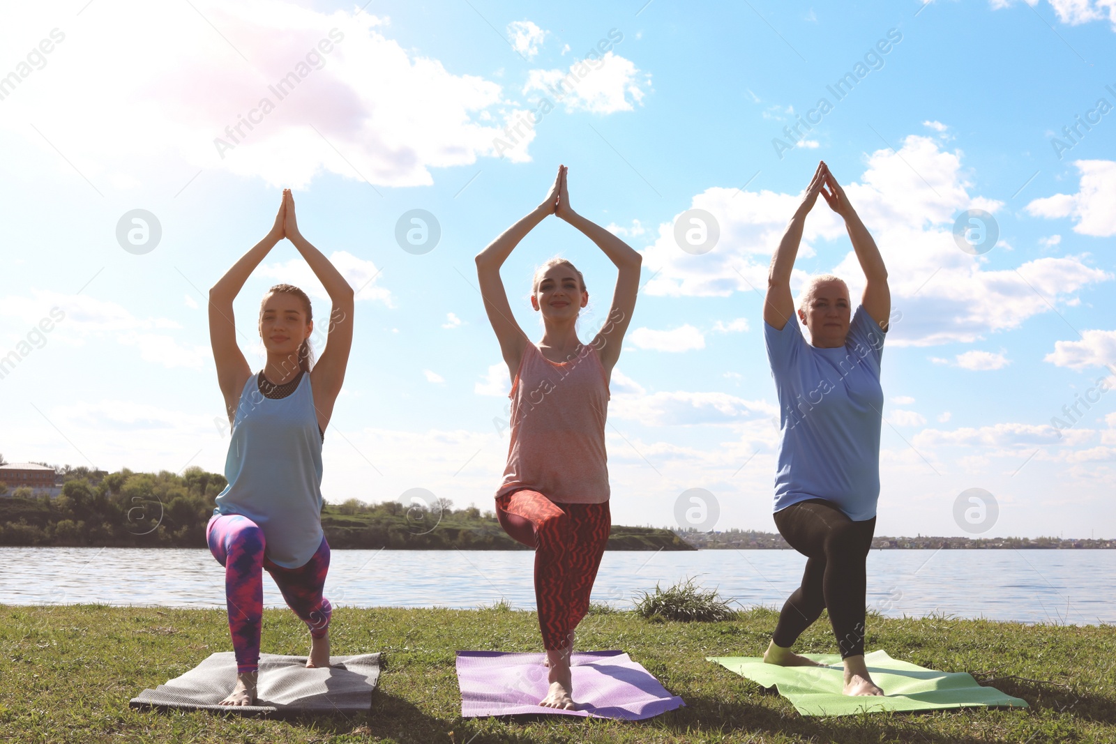 Photo of Group of women practicing yoga near river on sunny day