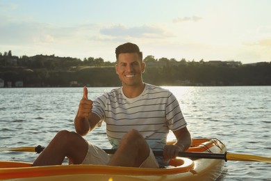 Photo of Happy man showing thumb up while kayaking on river. Summer activity