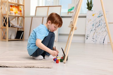 Photo of Little boy painting in studio. Using easel to hold canvas