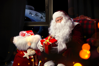 Image of Santa Claus with Christmas gifts in armchair near window indoors