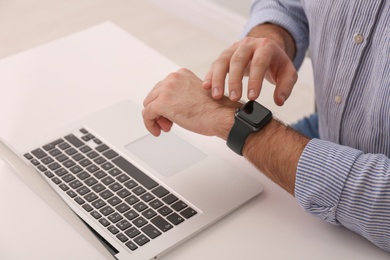 Young man using smart watch at table in office, closeup