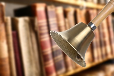 Image of Golden school bell with wooden handle and blurred view of books on shelves in library