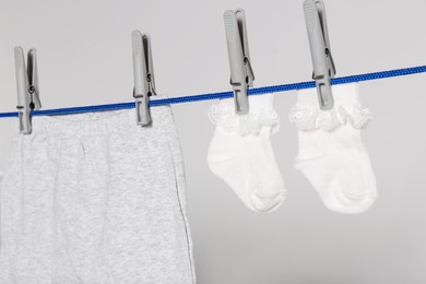 Photo of Different baby clothes drying on laundry line against light background, closeup