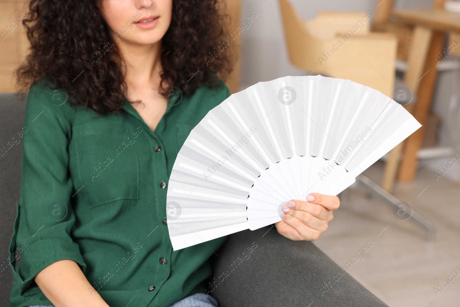 Photo of Woman with white hand fan on sofa at home, closeup