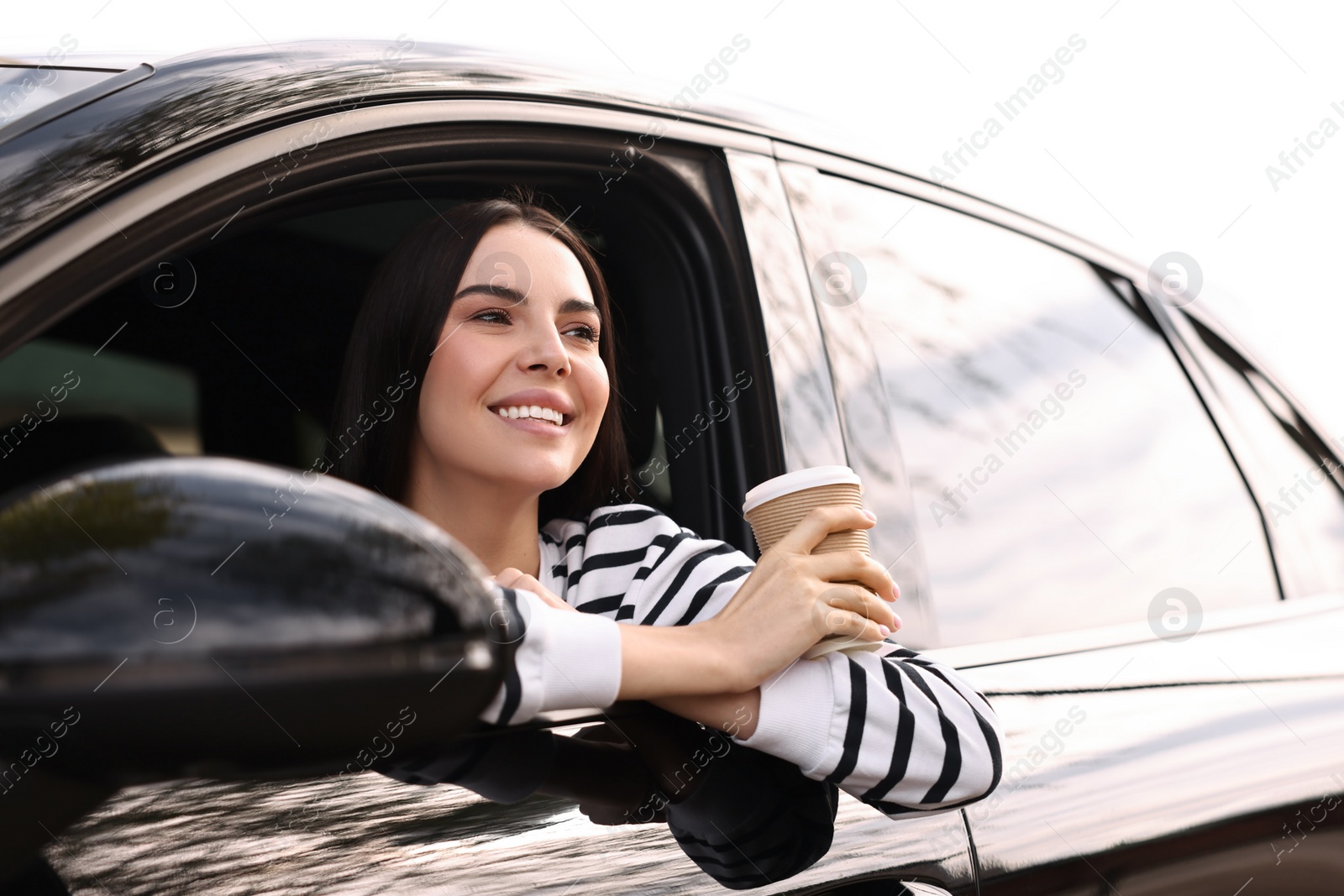 Photo of Young woman with cup of coffee sitting inside her modern car