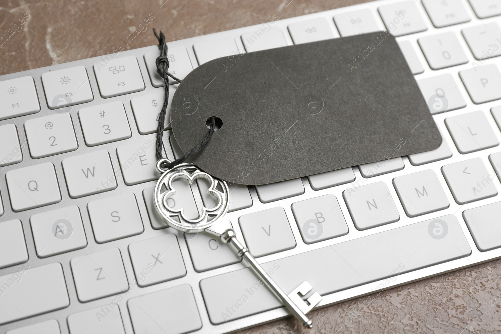 Photo of Vintage key with blank tag and keyboard on grey table, closeup. Keyword concept