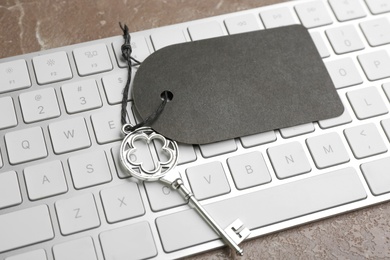 Vintage key with blank tag and keyboard on grey table, closeup. Keyword concept