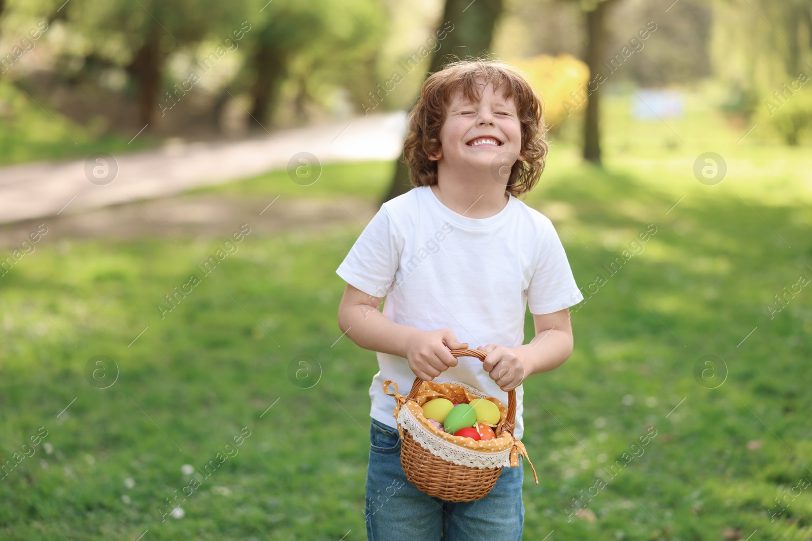 Photo of Easter celebration. Cute little boy holding wicker basket with painted eggs outdoors
