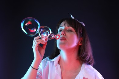 Photo of Portrait of happy woman blowing bubbles on dark background