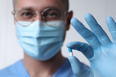 Photo of Doctor holding pill on light background, selective focus. Space for text