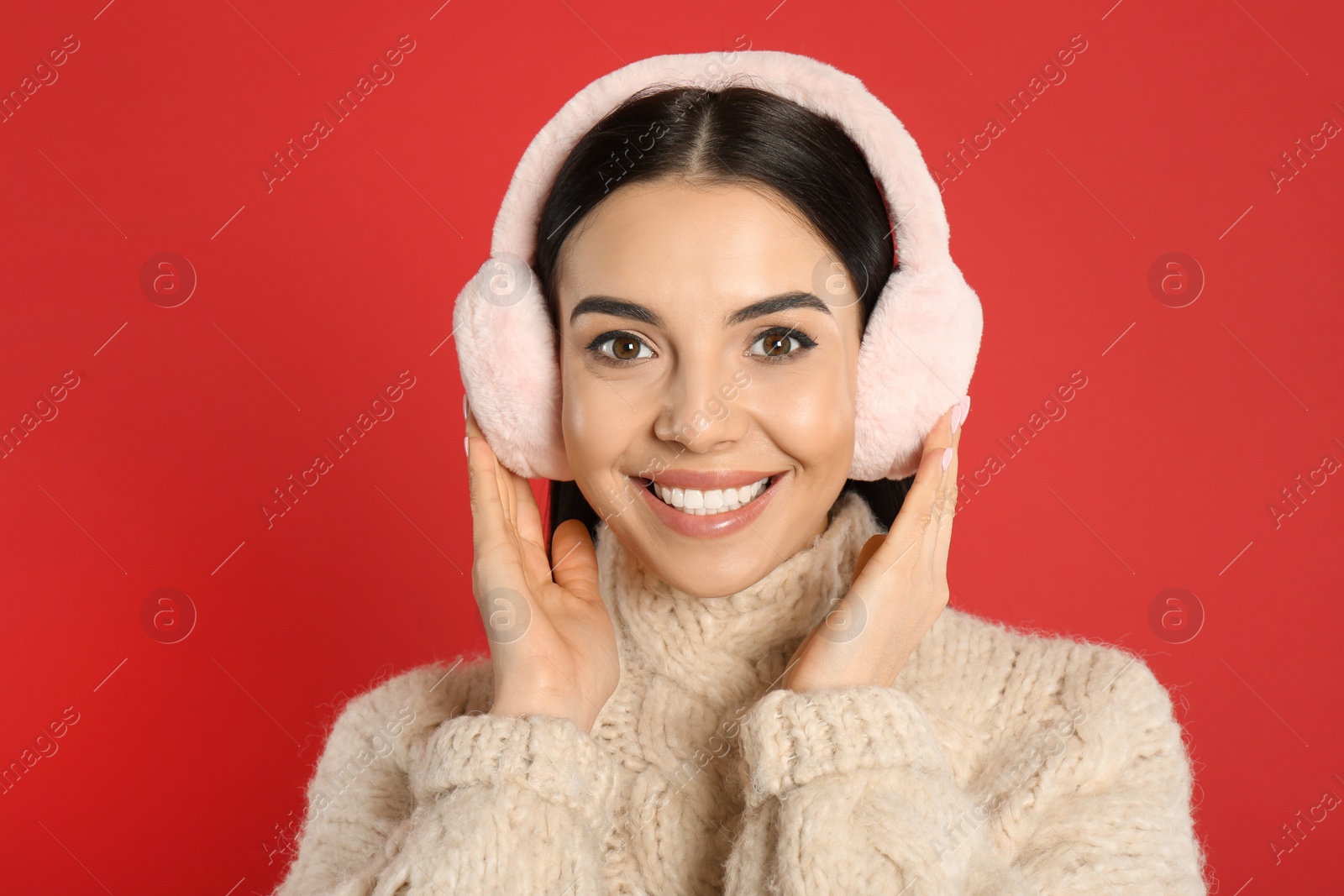 Photo of Beautiful young woman wearing earmuffs on red background