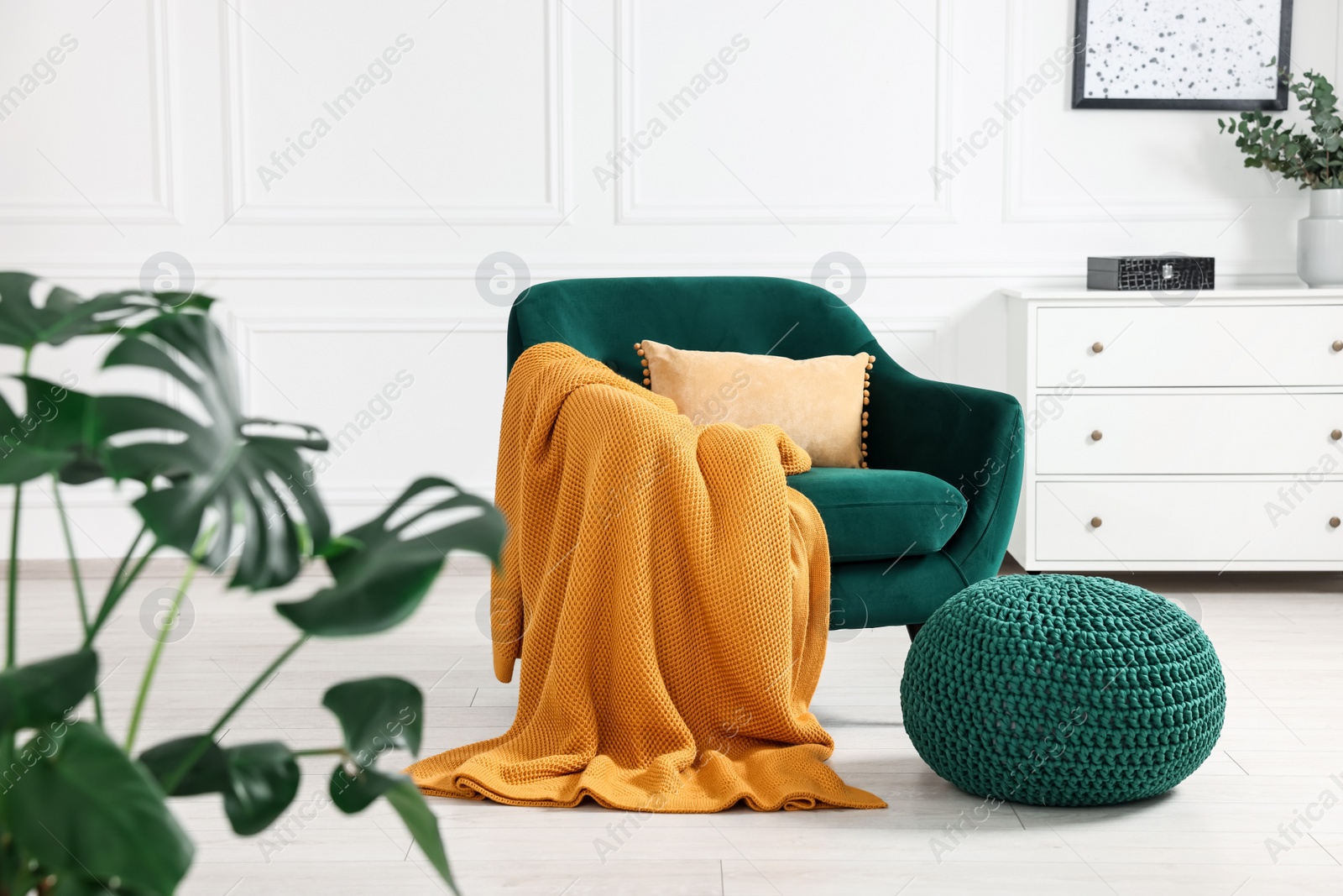 Photo of Comfortable armchair with blanket, ottoman and chest of drawers in room