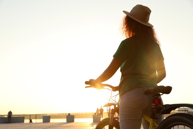 Photo of Young African-American woman with bicycle on city waterfront at sunset