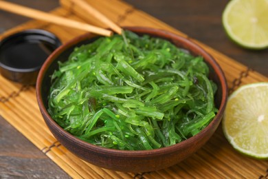 Photo of Tasty seaweed salad in bowl served on wooden table, closeup