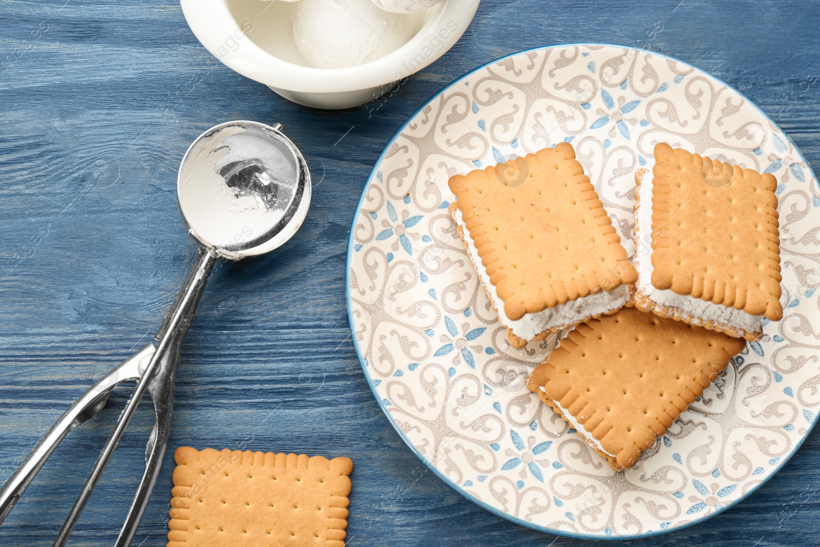 Photo of Sweet delicious ice cream cookie sandwiches served on blue wooden table, flat lay