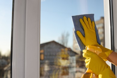 Young woman cleaning window glass with rag and detergent at home, closeup. Space for text