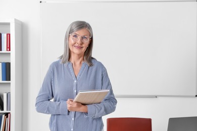 Photo of Portrait of professor with notebook near whiteboard in classroom, space for text