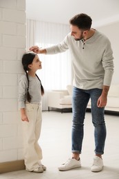Father measuring daughter's height near white brick pillar at home