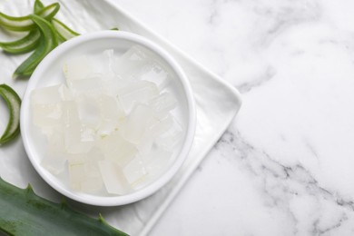 Photo of Aloe vera gel and slices of plant on white marble table, top view. Space for text