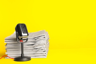 Photo of Newspapers and vintage microphone on yellow background, space for text. Journalist's work