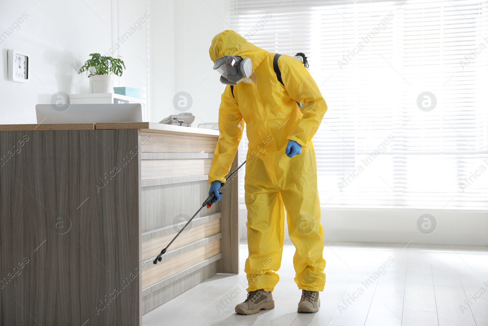 Photo of Employee in protective suit sanitizing office. Medical disinfection