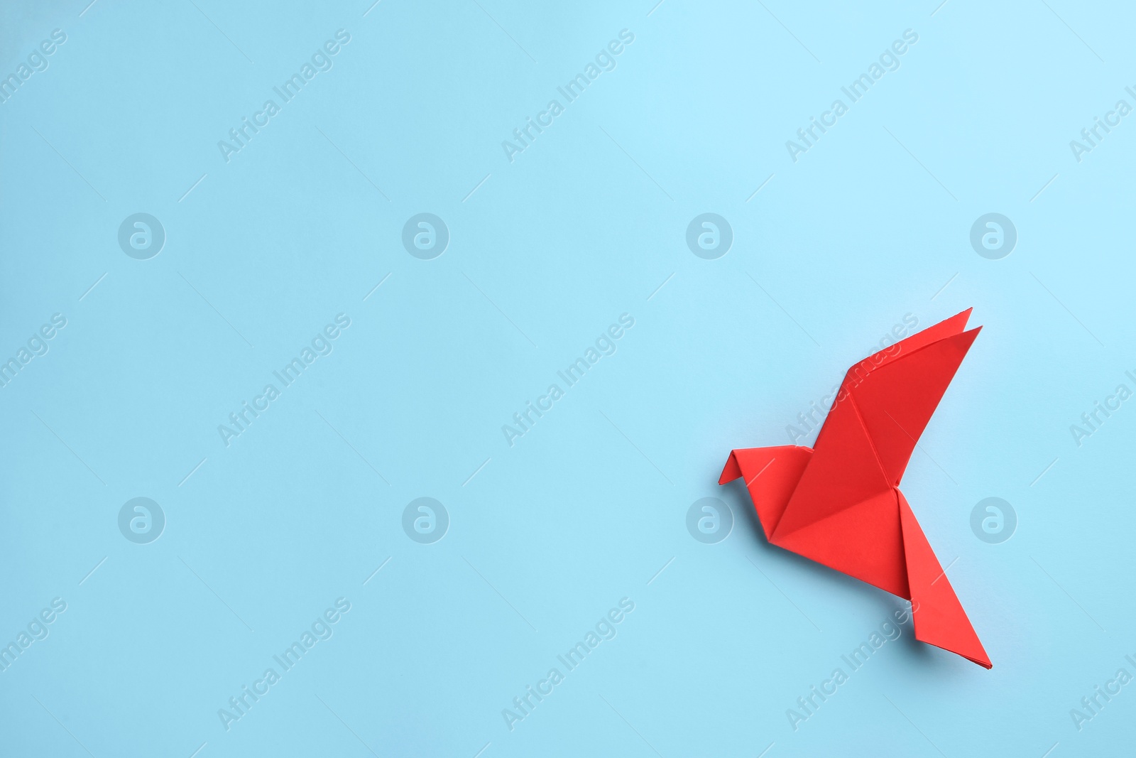 Photo of Origami art. Beautiful handmade paper bird on light blue background, top view. Space for text