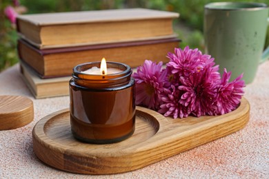 Photo of Burning candle and chrysanthemum flowers on beige textured table, closeup