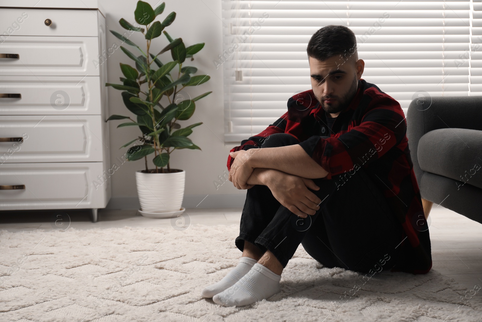 Photo of Sad man sitting on floor at home. Space for text