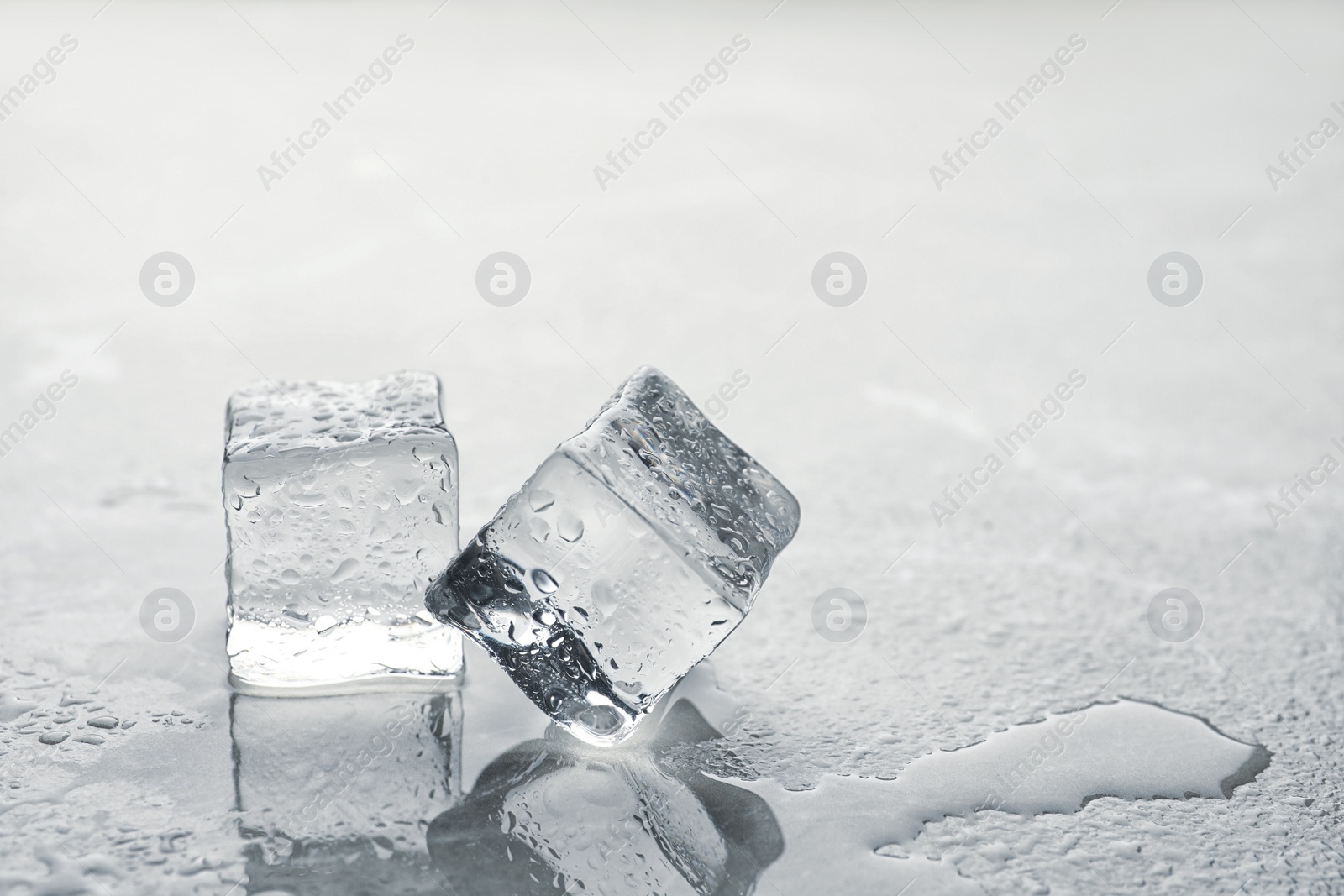 Photo of Crystal clear ice cubes with water drops on metal surface. Space for text