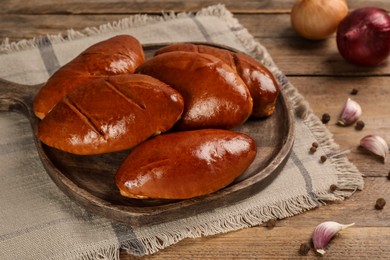 Photo of Delicious baked pirozhki, garlic and peppercorns on wooden table