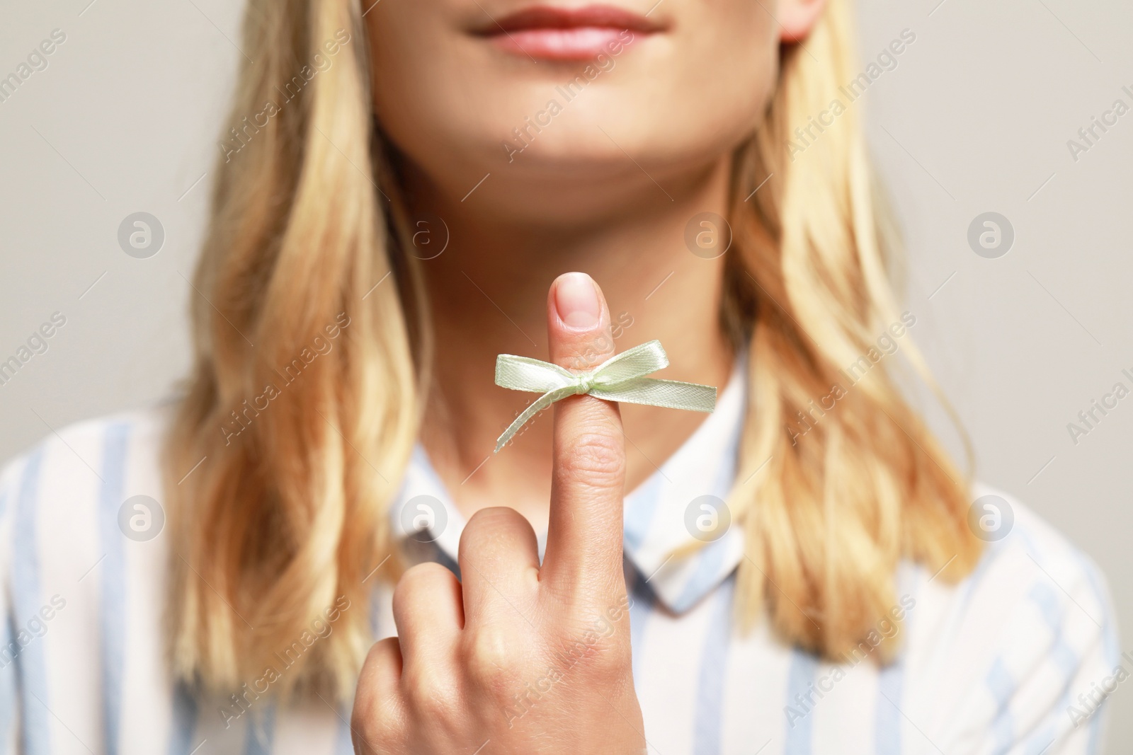 Photo of Woman showing index finger with tied bow as reminder against grey background, focus on hand