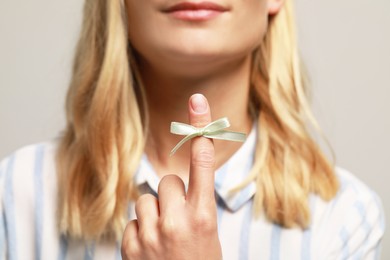 Woman showing index finger with tied bow as reminder against grey background, focus on hand