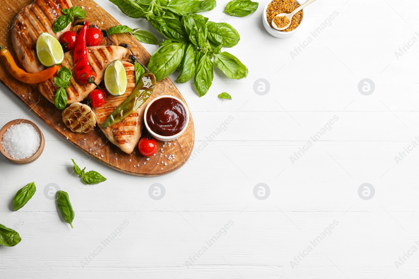 Photo of Tasty grilled chicken fillets with sauce and vegetables on white wooden table, flat lay. Space for text