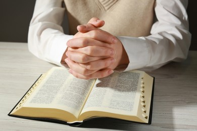 Photo of Woman praying over Bible at white wooden table, closeup