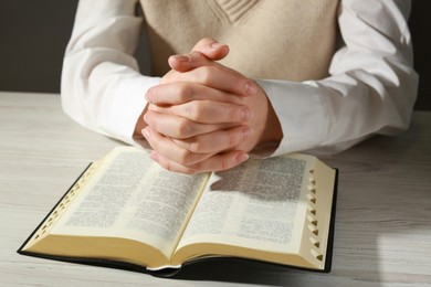 Woman praying over Bible at white wooden table, closeup